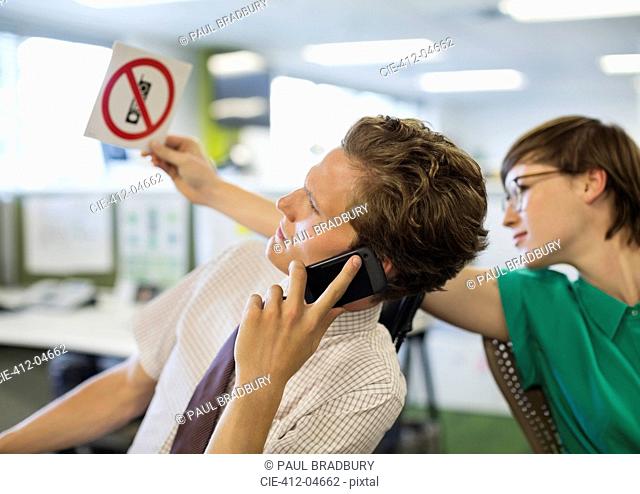 Businesswoman showing ‘no cell phones’ sign to colleague