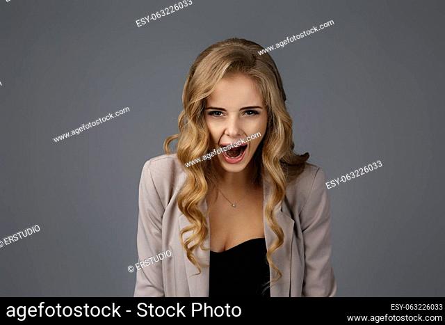Portrait of young angry woman screaming on gray background