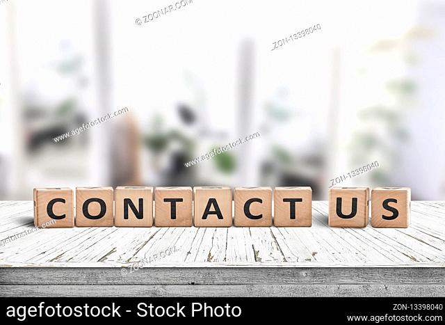 Contact us sign on a wooden desk in a bright living room with green plants