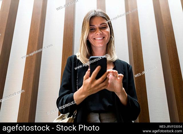 Smiling businesswoman using smart phone in front of wall