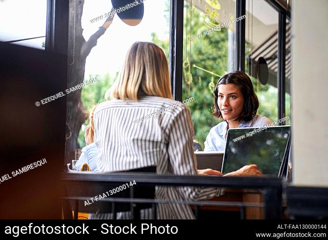 Mid-shot of two female entrepreneurs discussing business while working at cafe