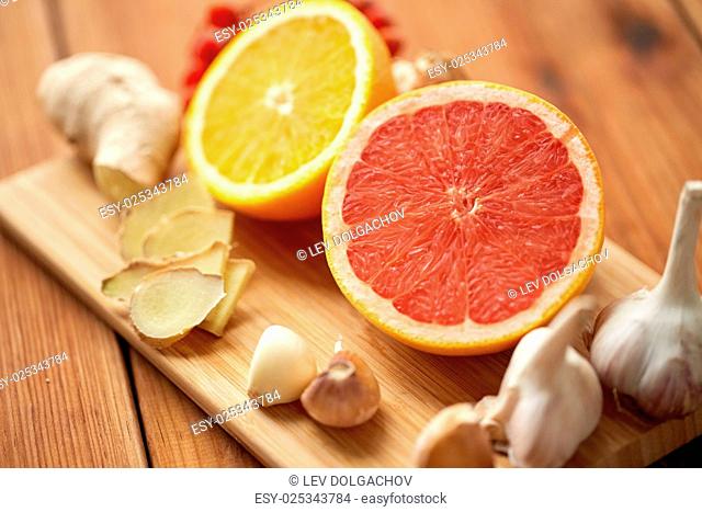 traditional medicine, cooking and ethnoscience concept - ginger, orange, grapefruit and garlic on wooden board