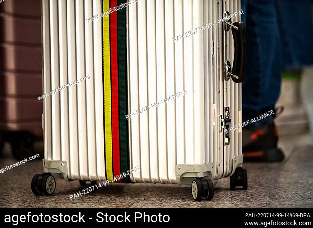 14 July 2022, Lower Saxony, Hanover: A suitcase with a luggage belt in Germany colors stands at a check-in counter at Hannover Airport