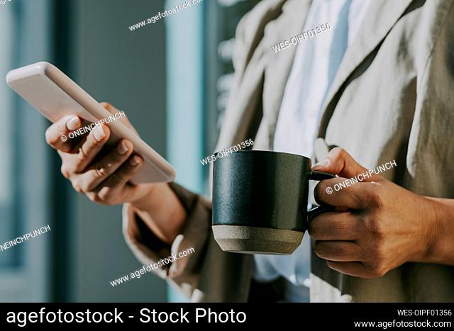 Woman holding coffee cup while using mobile phone during sunny day