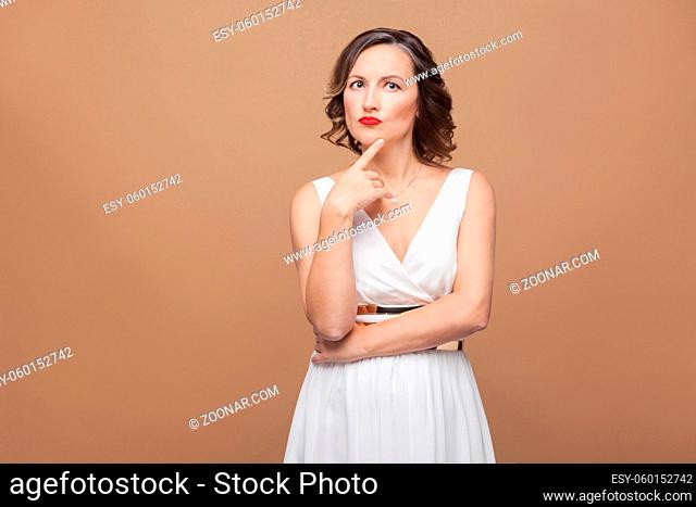 Beautiful middle aged woman thinking and puzzled. Emotional expressing woman in white dress, red lips makeup and dark curly hairstyle