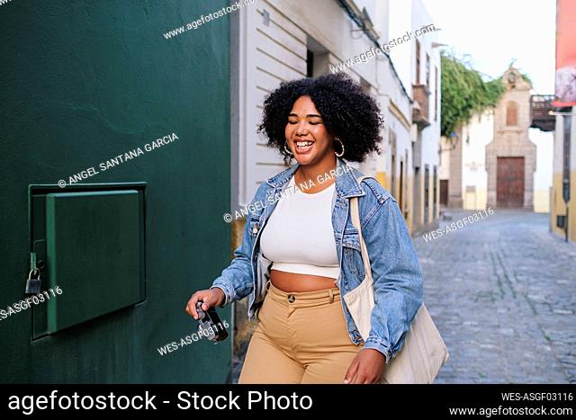 Happy young woman with camera walking in alley