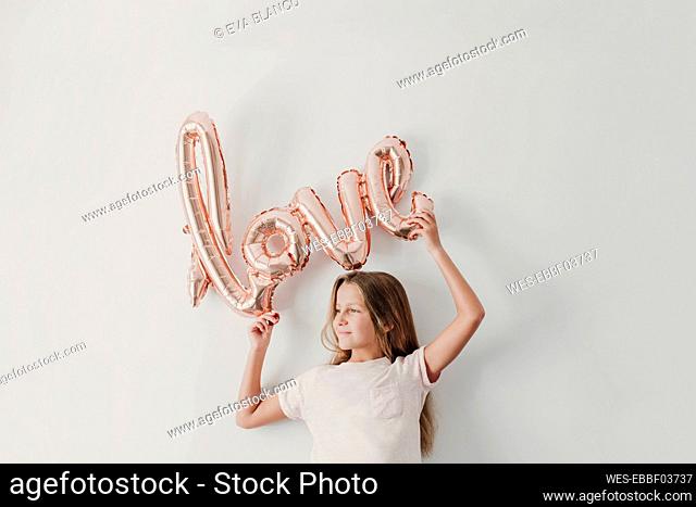 Smiling girl holding love balloon while standing in front of wall