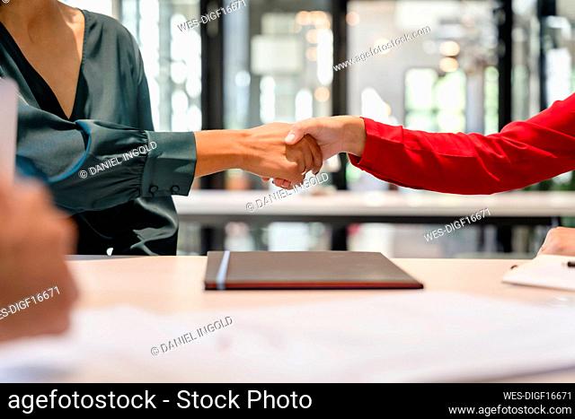 Businesswomen doing handshake at desk
