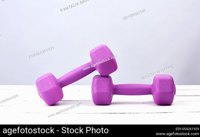 pair of purple plastic dumbbells for sports on a white wooden background, copy space. Fitness training. Healthy lifestyle
