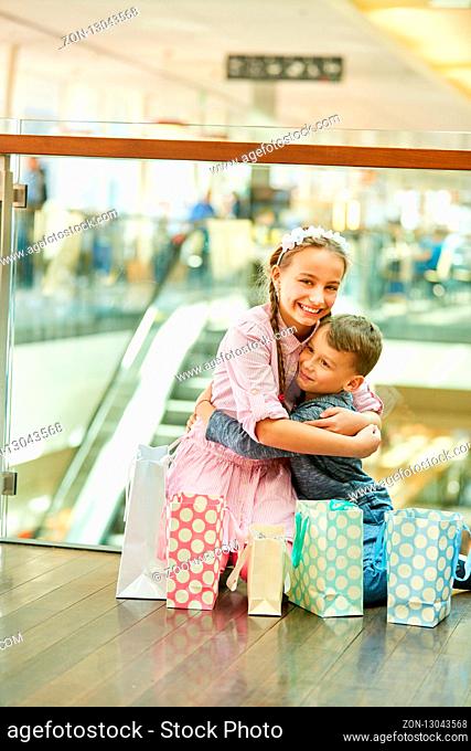 Bruder und Schwester im Einkaufszentrum mit vielen Einkaufstüten umarmen sich