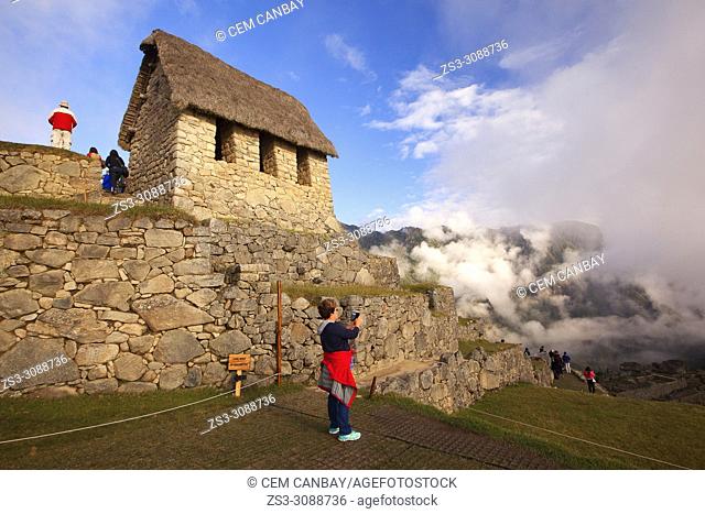 Tourists at the Industrial Sector in front of the Hut of the Caretaker of the Funerary Rock in the early morning light, Machu Picchu, Cusco Region, Peru