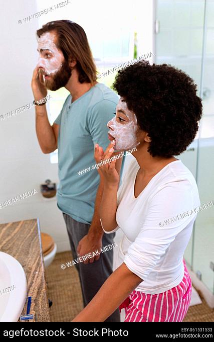 Diverse couple standing in bathroom wearing beauty masks