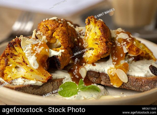 High angle close up of roasted cauliflower with yoghurt and sesame seeds on toasted sourdough bread in a cafe