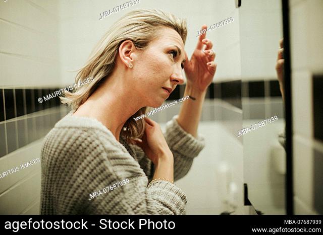 Woman in the bathroom, looks critically at her reflection
