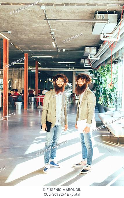 Portrait of male adult hipster twins holding digital tablet and laptop in office
