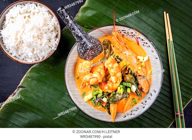 Traditional Thai kaeng phet red curry with king prawns and rice as top view in a bowl on a banana leaf
