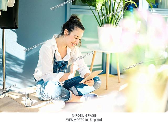 Smiling young freelancer sitting on the floor in her studio using tablet