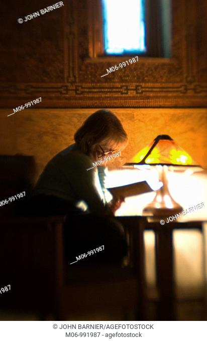 Woman reading in a darkened room, sitting by a lone lamp