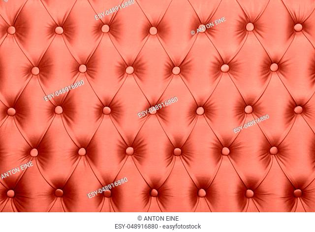 Coral toned pink leather capitone textile background, retro Chesterfield style checkered soft tufted fabric furniture decoration with buttons, close up