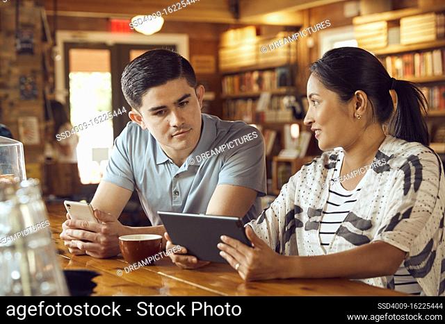 Young man and woman sitting at counter in cafe bookstore looking at tablet