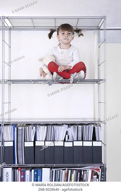 little girl seated high up in a bookshelf
