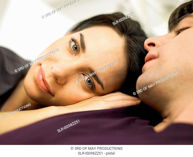 Young couple lying in bed, woman's head on man's shoulder