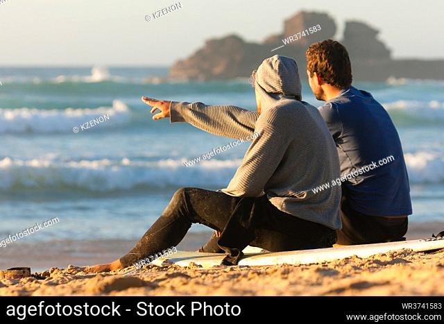 Two surfers sitting on their surf boards on the beach discussing the waves