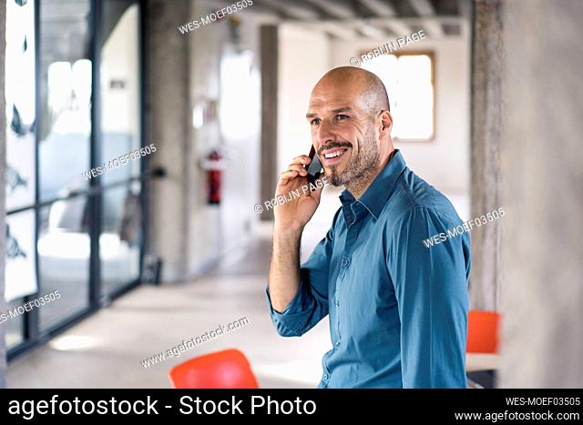 Smiling businessman talking on mobile phone while sitting on table at office