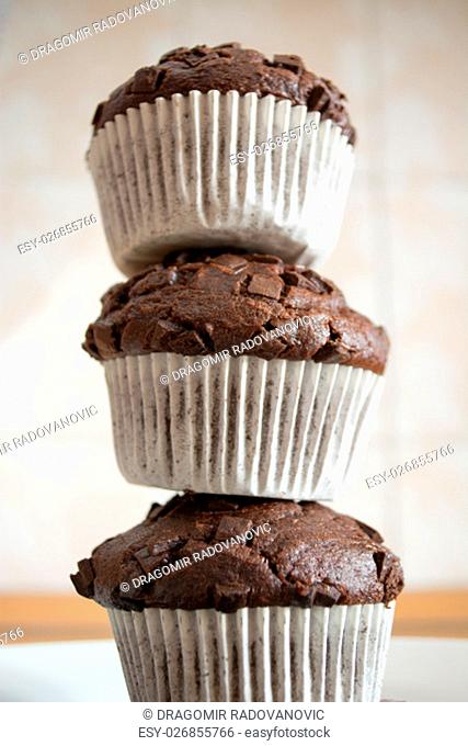 Three chocolate cupcakes stacked to form a tower in the kitchen