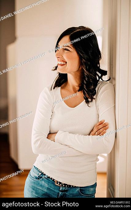 Smiling woman with arms crossed looking away while standing at home