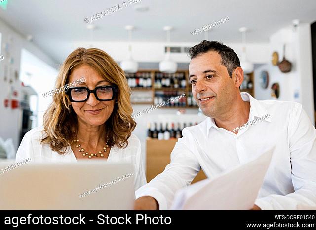 Smiling restaurant owner discussing over laptop with colleague