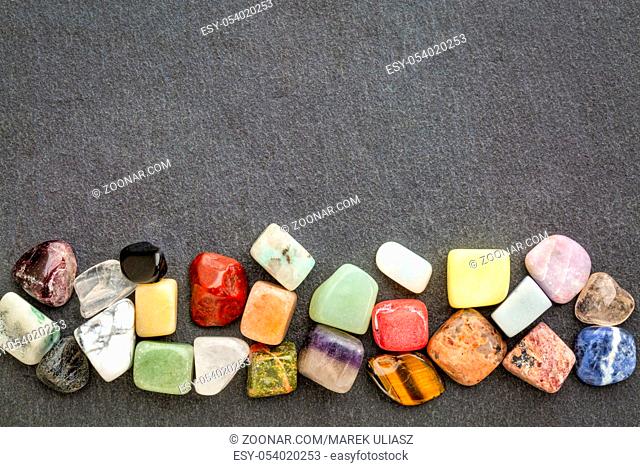 a row of polished, semiprecious, colorful gemstones against gray slate stone with a copy space