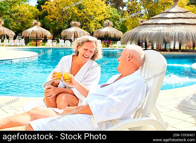 Glückliches Paar Senioren sitzt mit Orangensaft am Pool vom Hotel