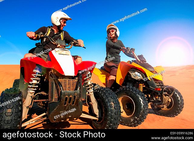 Happy couple of quad bikers laughing joyful, cheerful and fresh. Young active caucasian couple in outdoor activity driving quad ATV in Namib desert sunrise or...