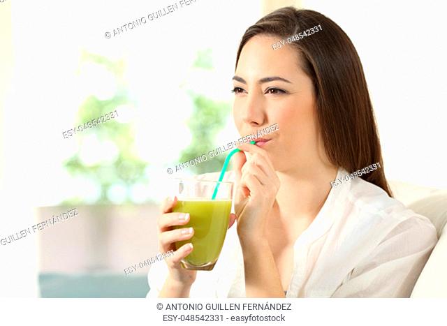 Girl drinking vegetable juice from a glass sipping a straw sitting on a couch in the living room at home