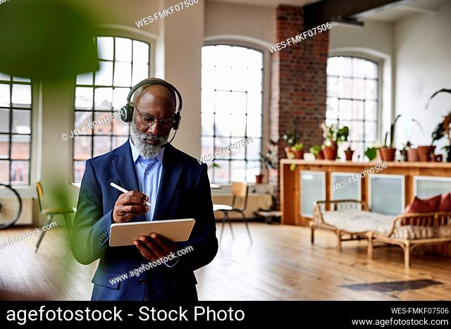 Businessman with headset using digitized pen on tablet PC at home