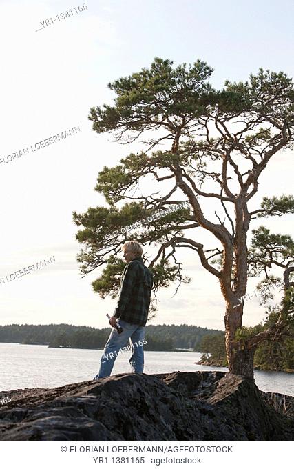 Young man with beer bottle, standing by lake