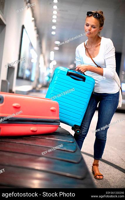 Young woman with her luggage at an international airport, waiting for her luggage to arrive at the baggage claim zone