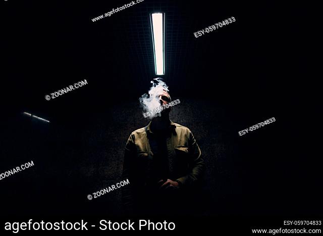 Portrait of young caucasian man smoking e-cigarette in dark with line light
