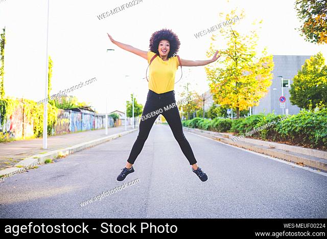 Happy young woman with afro hairdo jumping on a street in the city
