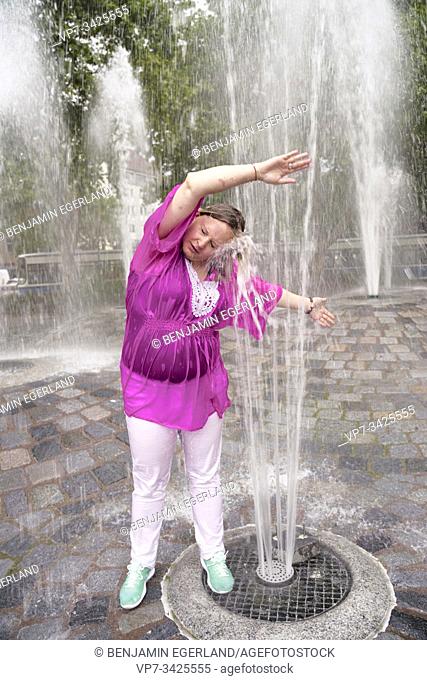 Woman under fountain water spray, Munich, Germany