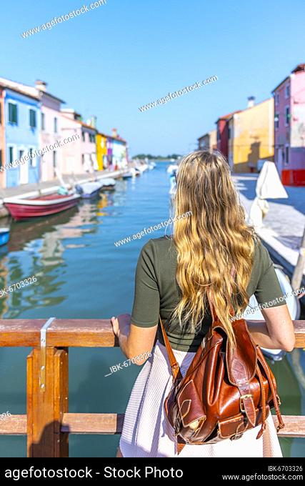 Young woman in front of colorful houses, canal with boats and colorful house facades, Burano Island, Venice, Veneto, Italy, Europe