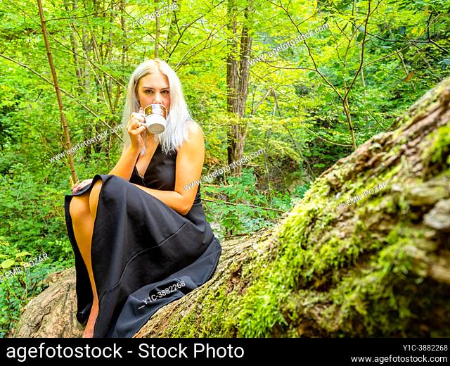 Attractive blonde woman on a tree drinking coffee