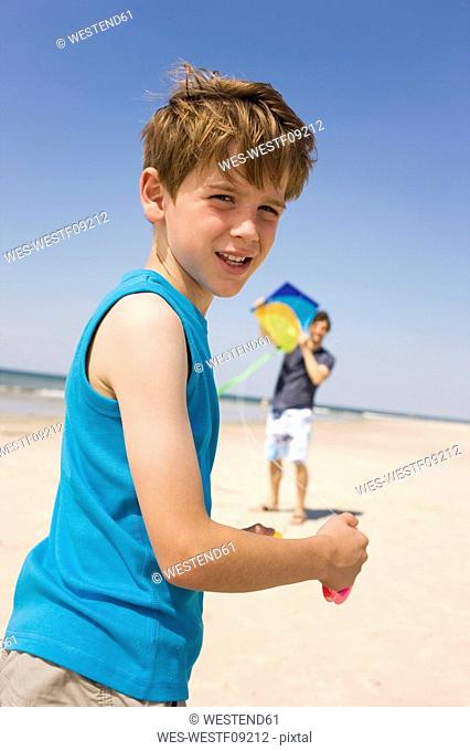 Germany, Baltic sea, Father with son 8-9 flying kite on beach