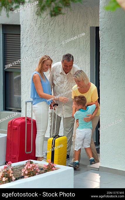 A woman with her son saying farewell to her parents before leaving with two bright suitcases