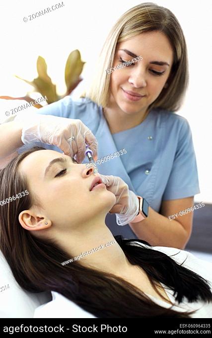 Professional beautician injecting hyaluronic acid near eyes of woman during anti aging procedure in beauty clinic