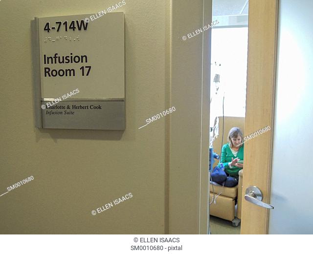 Caucasian woman seen through the door of a hospital infusion room getting a chemotherapy drug treatment for cancer