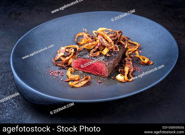 Modern style traditional dry aged sliced beef tenderloin with fried onion rings and red wine salt served as close-up on a design plate