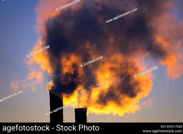 Harmful emissions from the plant pipe against the background of the setting sun