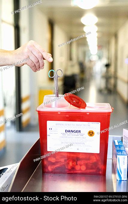 19 December 2019, Baden-Württenberg, Freiburg: An employee drops a pair of scissors made of non-reusable medical stainless steel into a container for collecting...